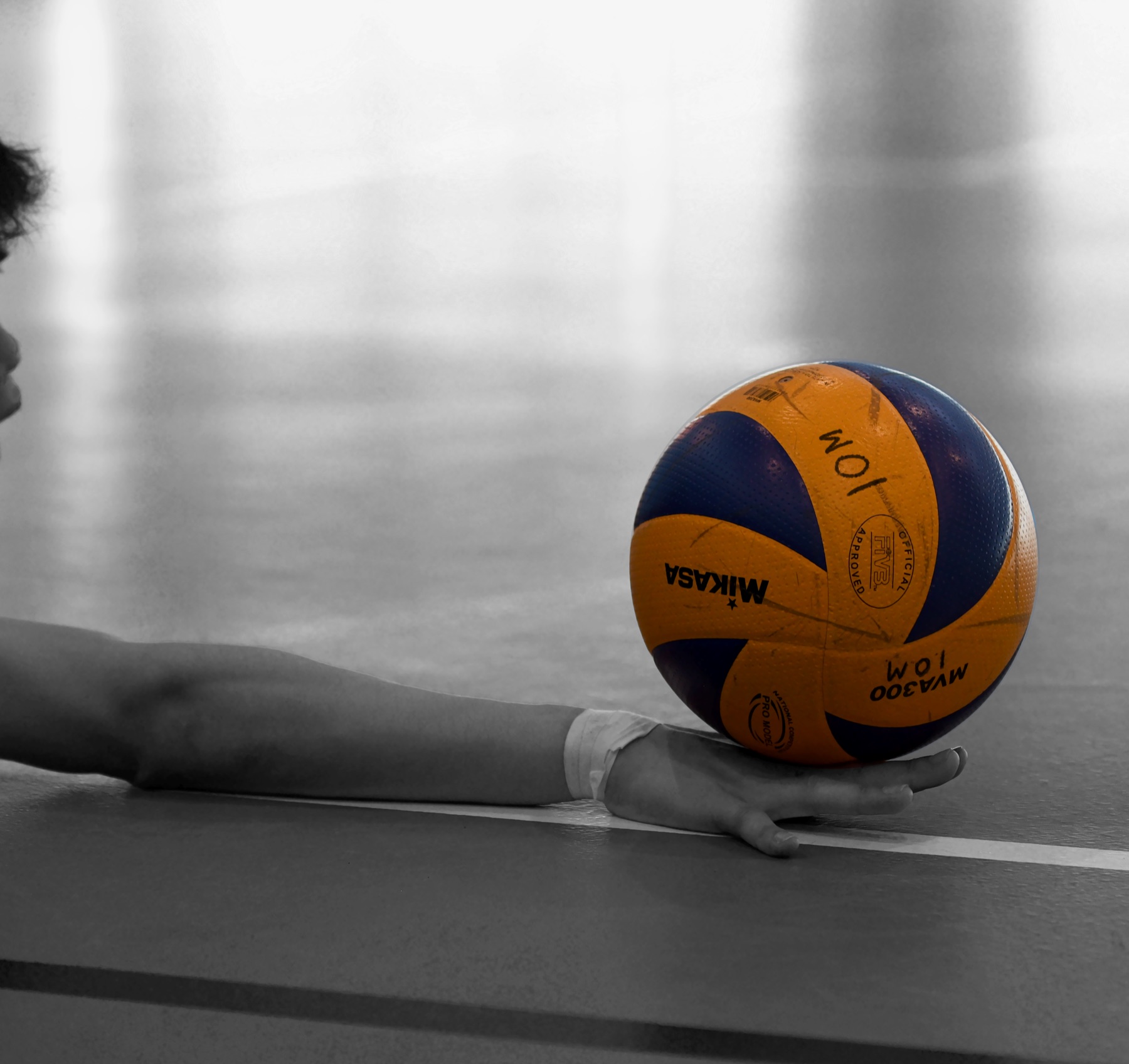 A volleyball resting on the court beneath an outstretched arm