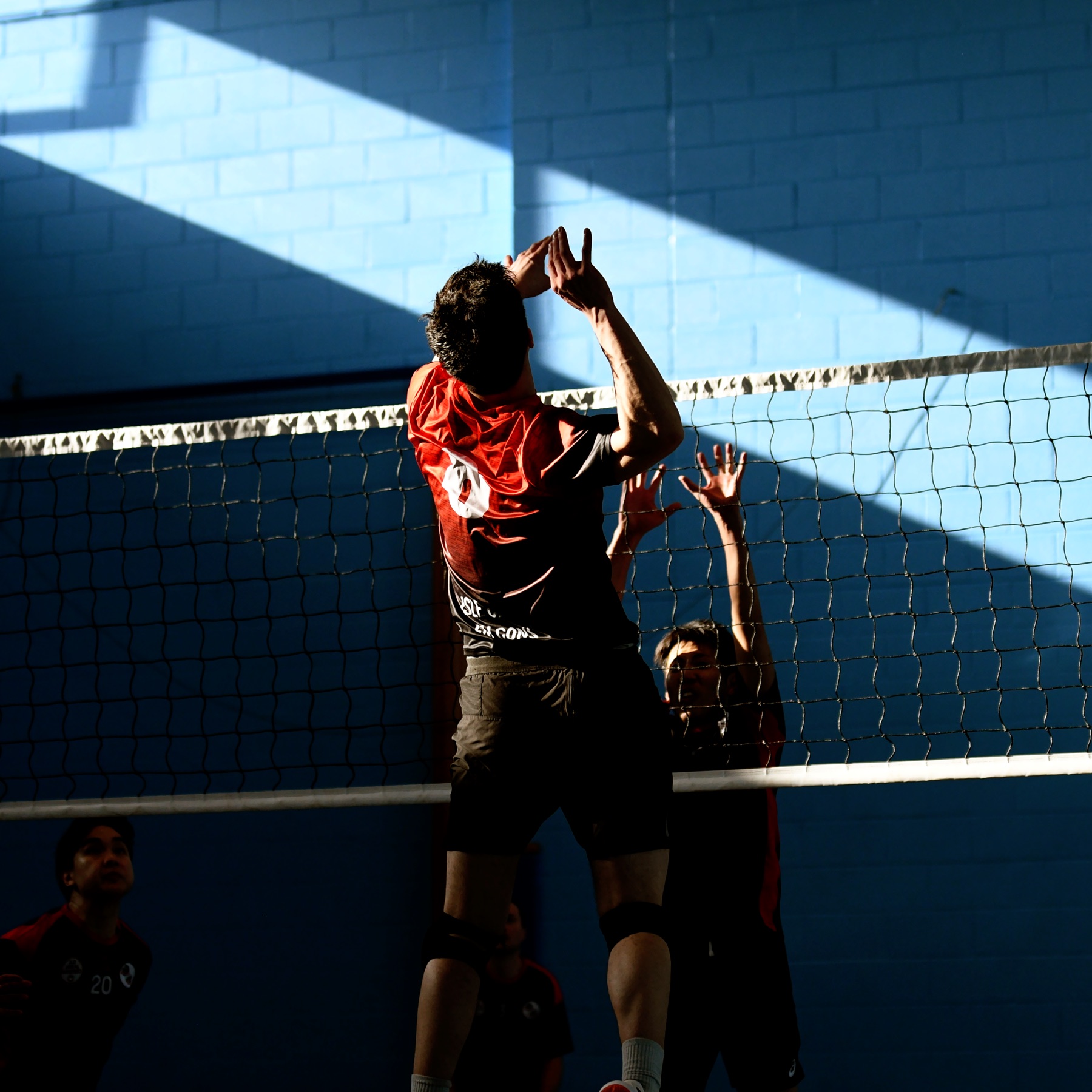 A player rising to attack at the net in dramatic side light